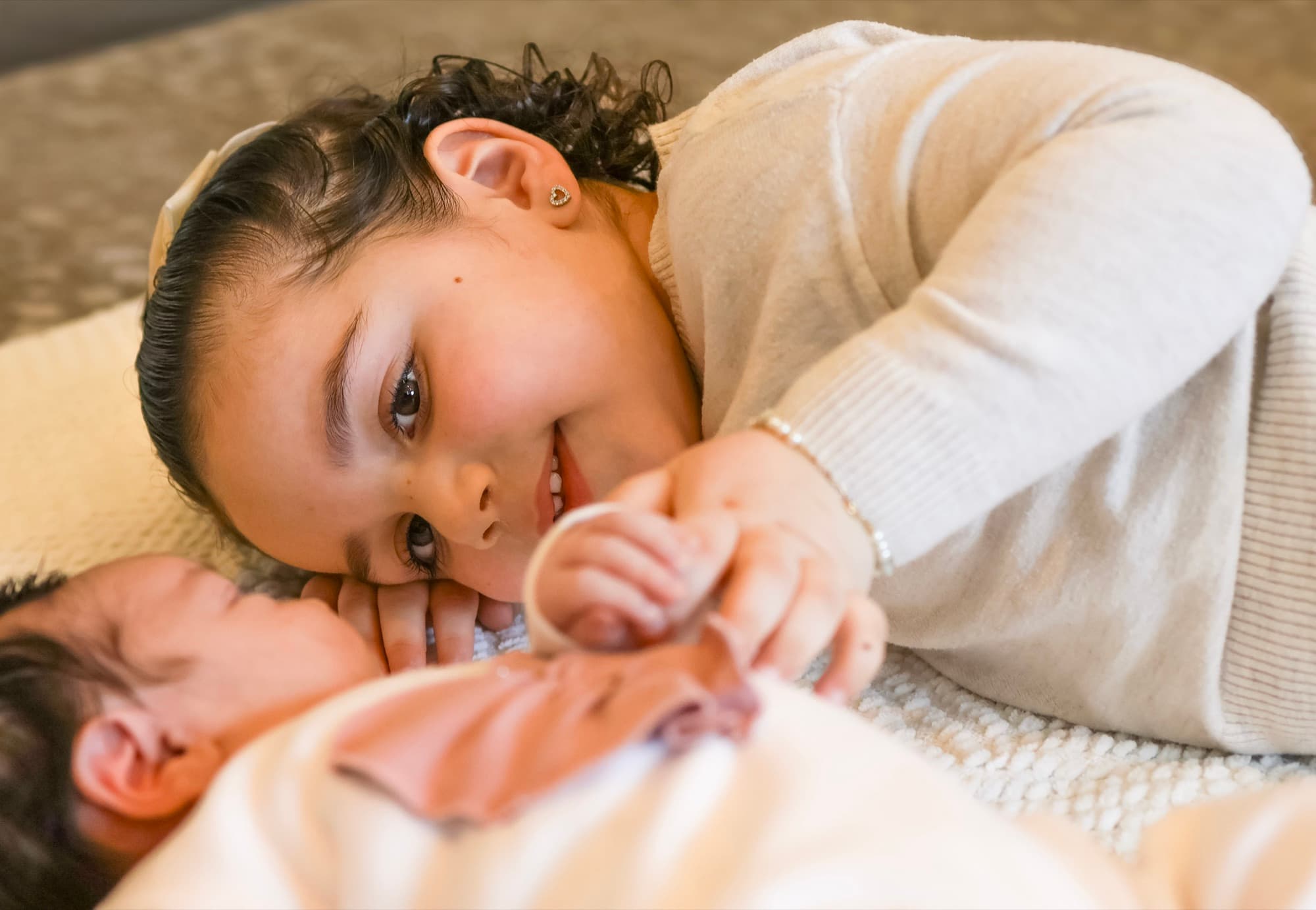 Big sister lying next to newborn — tender sibling moment