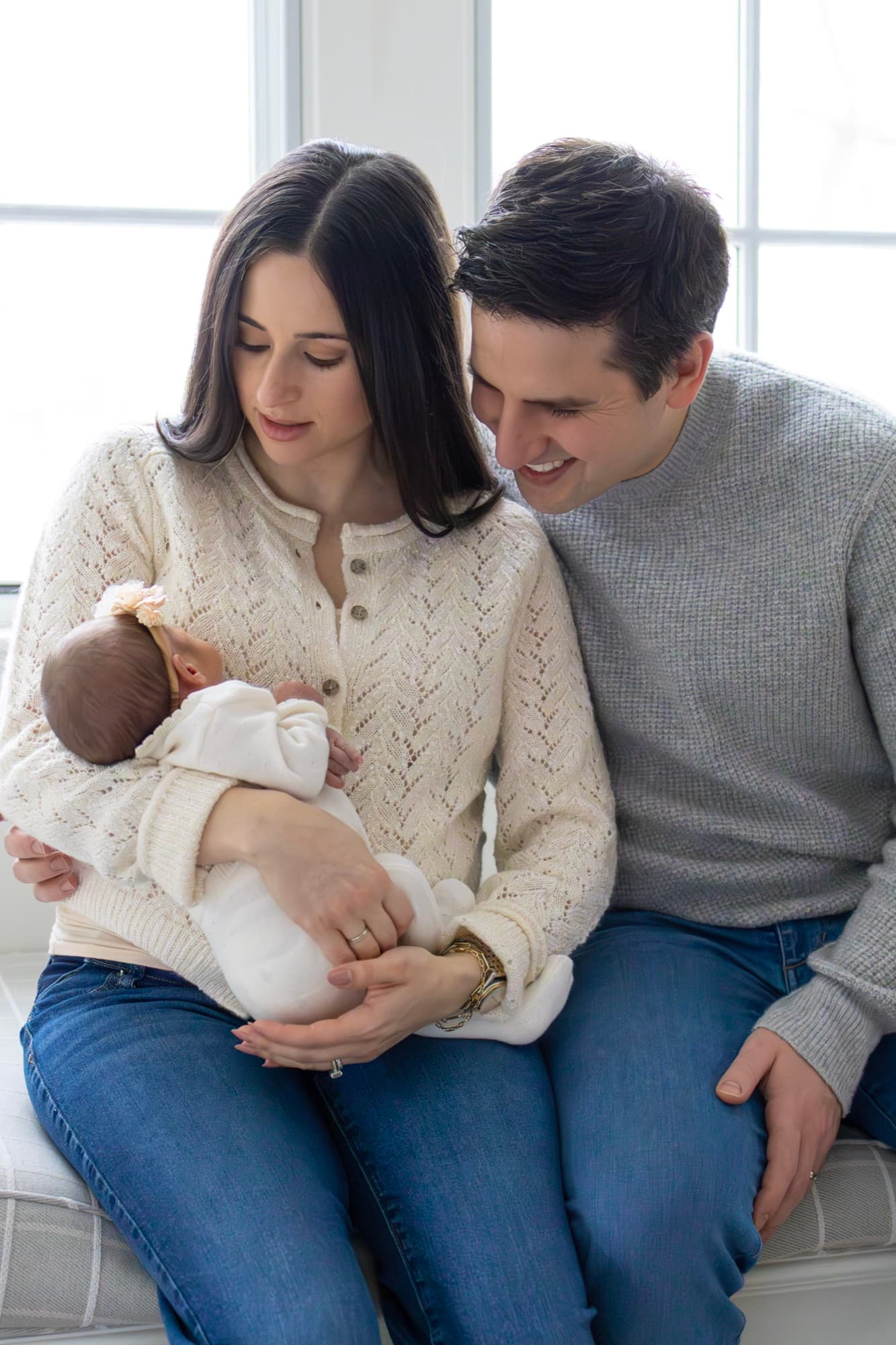 Parents holding newborn by window — natural light newborn photography