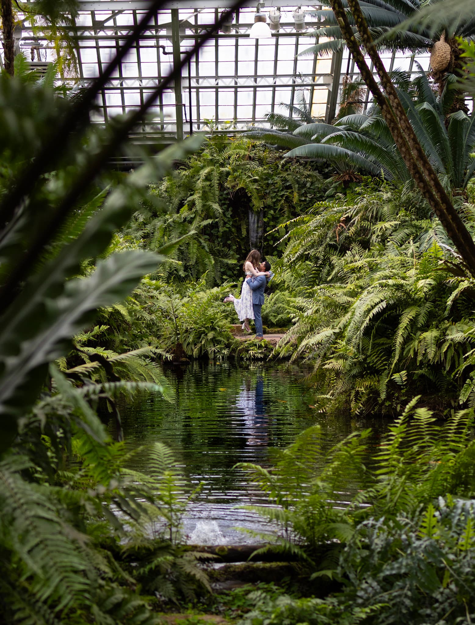 Wide engagement portrait of the couple by the indoor pond at Garfield Park Conservatory in Chicago