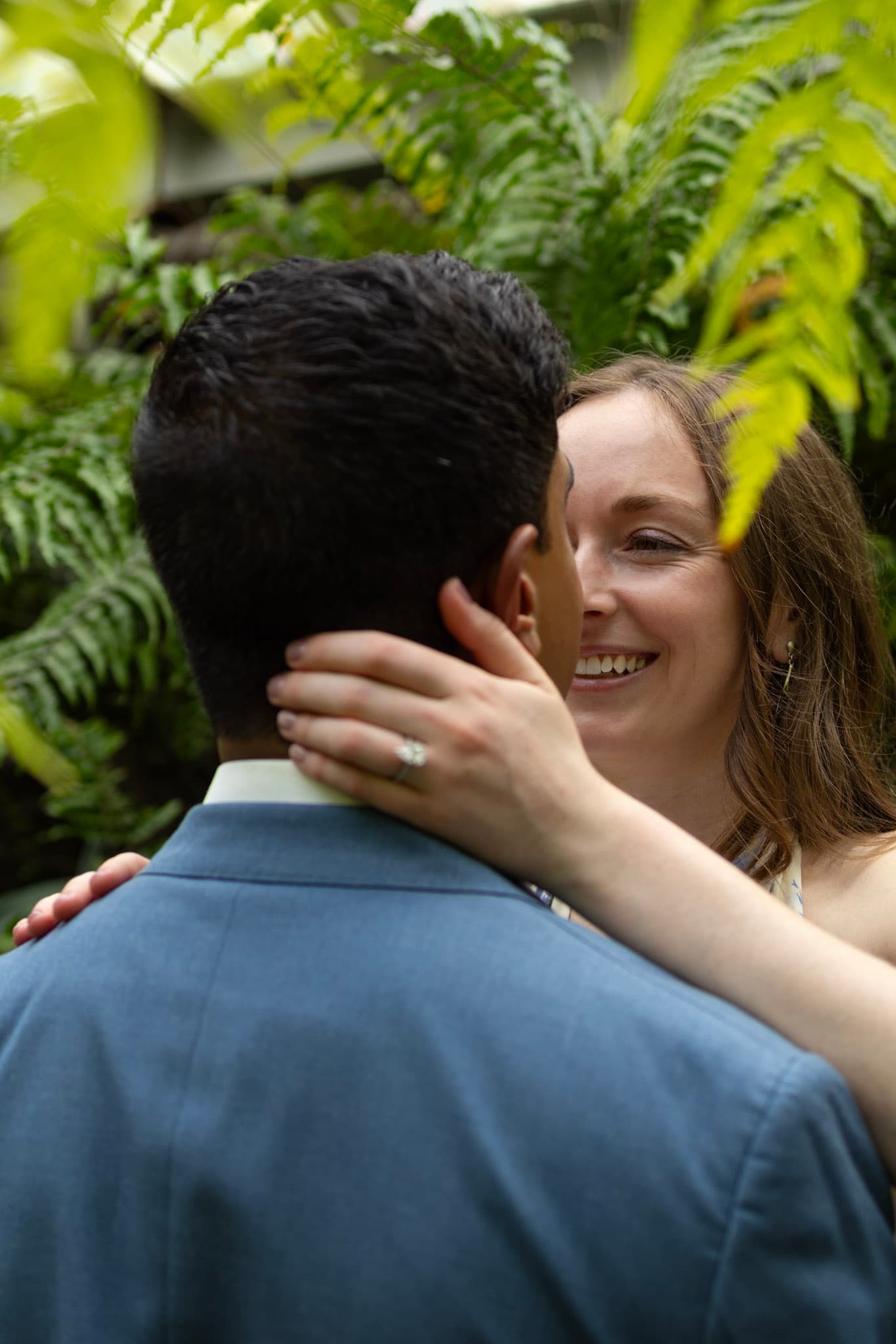 Close-up of engaged couple smiling among ferns during a Chicago conservatory photo session