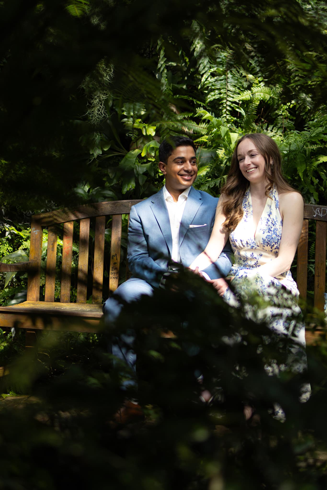 Couple seated on a bench framed by leafy shadows inside Garfield Park Conservatory