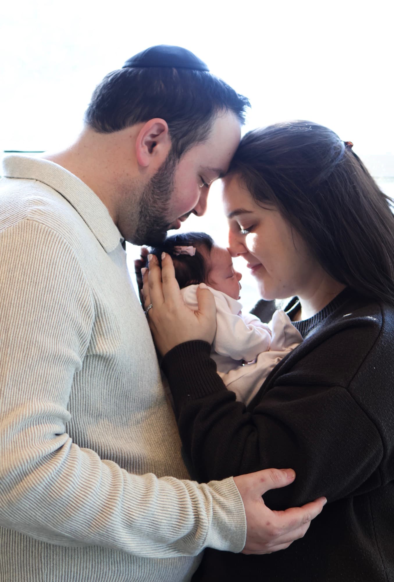 Parents holding newborn between them by window — intimate newborn photography