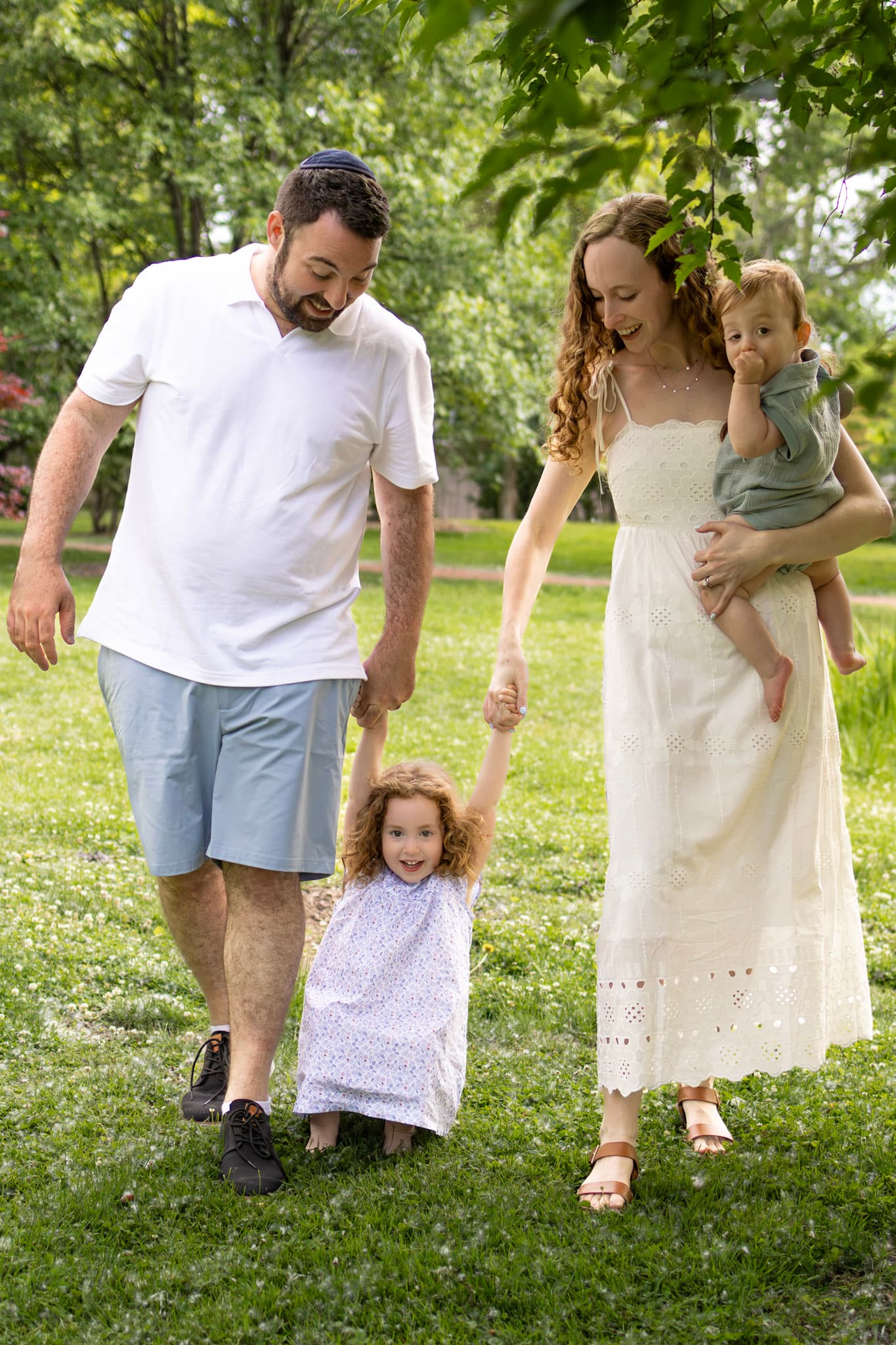 Family of four walking together holding hands across a green clearing during a Wilmette family photo session