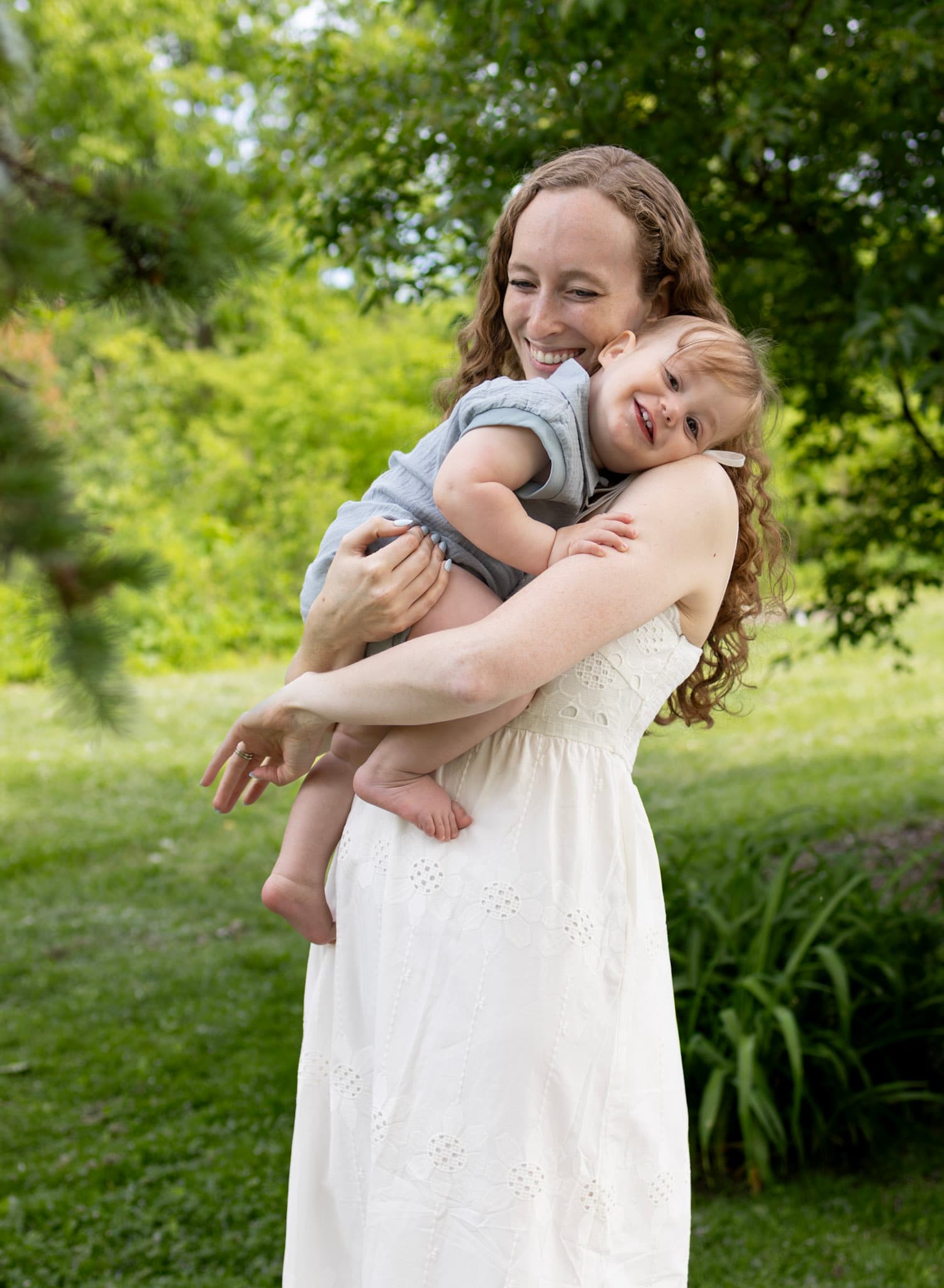 Mom in eyelet white dress hugging toddler son in green park setting at Keay Nature Center