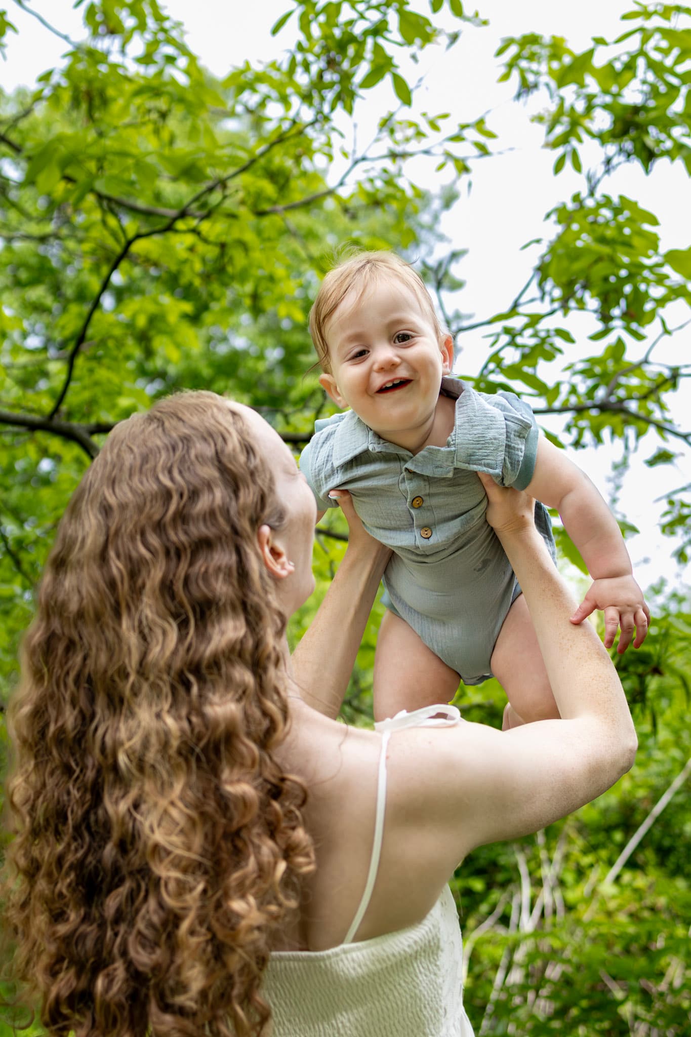 Mom lifting toddler son above her against a leafy green canopy during Keay Nature Center family photos