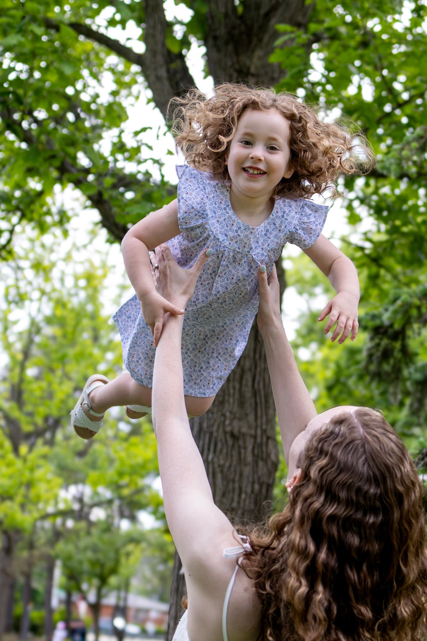 Mom lifting toddler daughter above her in a quiet woodland clearing at Keay Nature Center