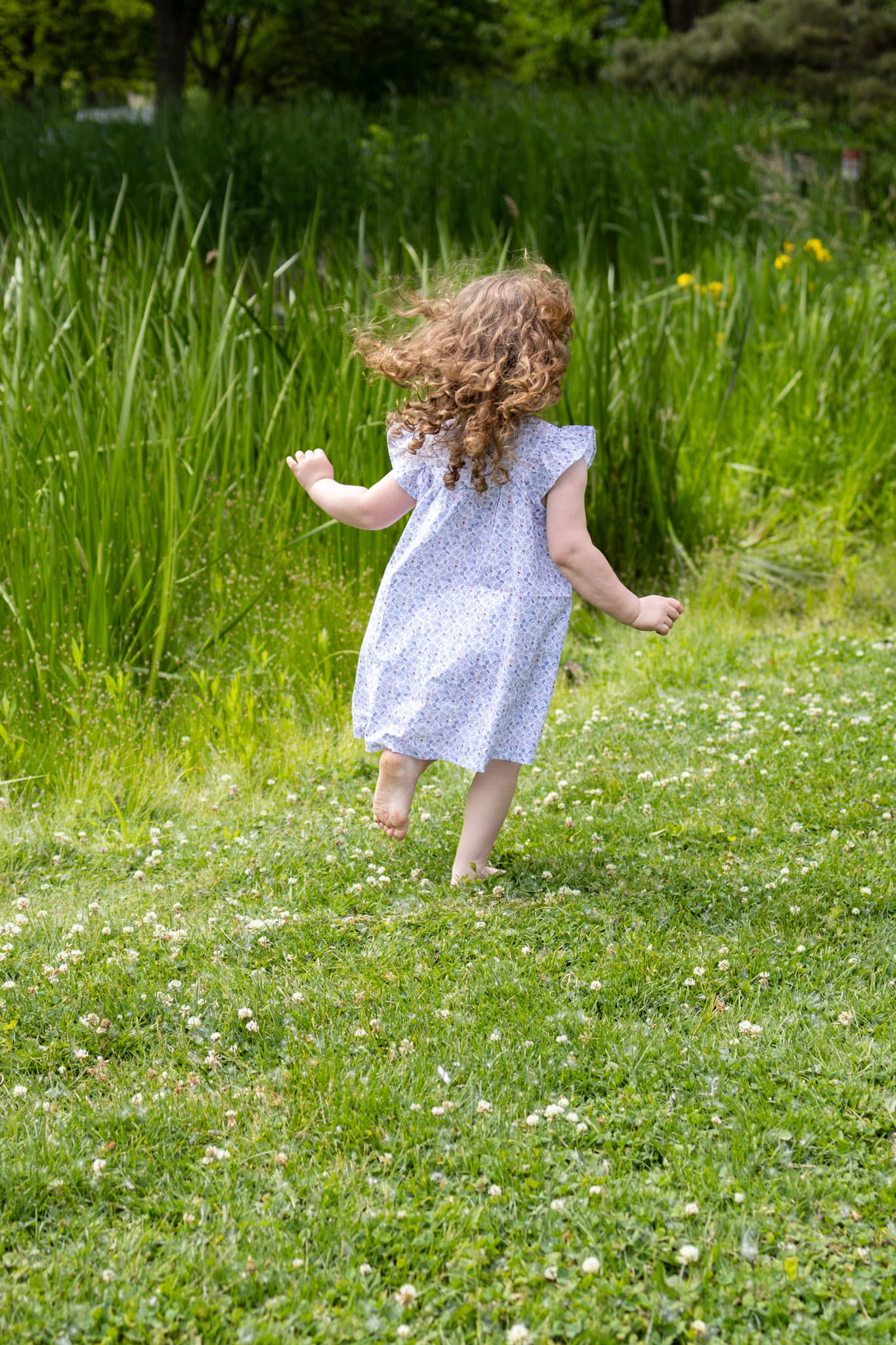 Young girl in floral dress running barefoot through tall grasses at Keay Nature Center in Wilmette