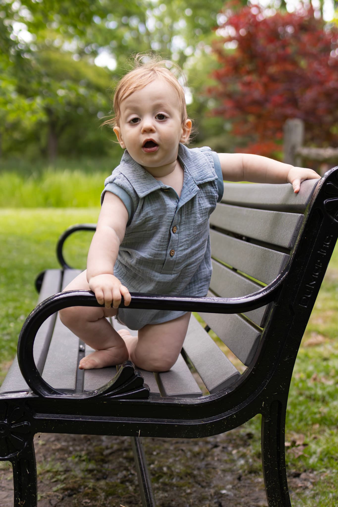 Toddler boy in blue romper exploring a park bench at Keay Nature Learning Center in Wilmette