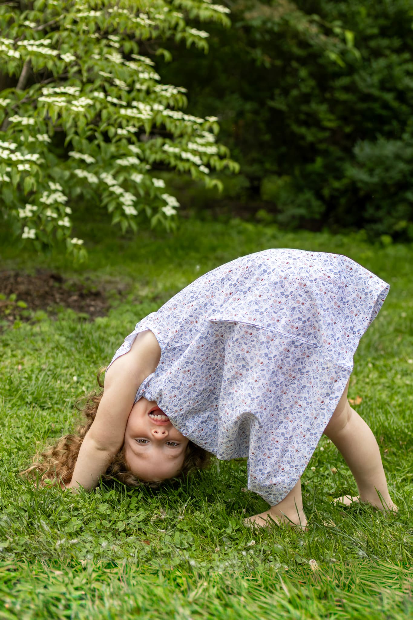 Playful candid of young girl peeking through her floral dress in the grass during a Wilmette family session