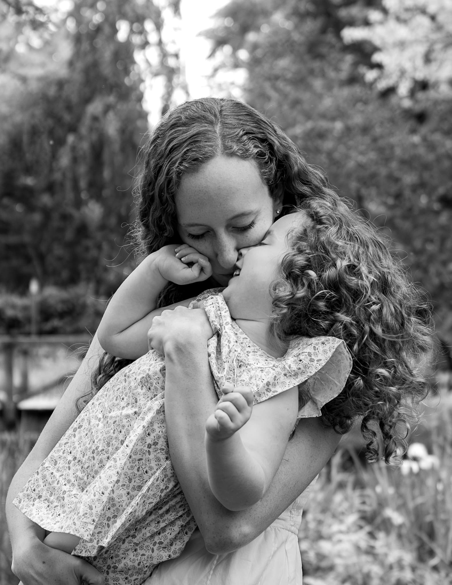 Black and white moment of mom kissing daughter outdoors during a Wilmette family photo session