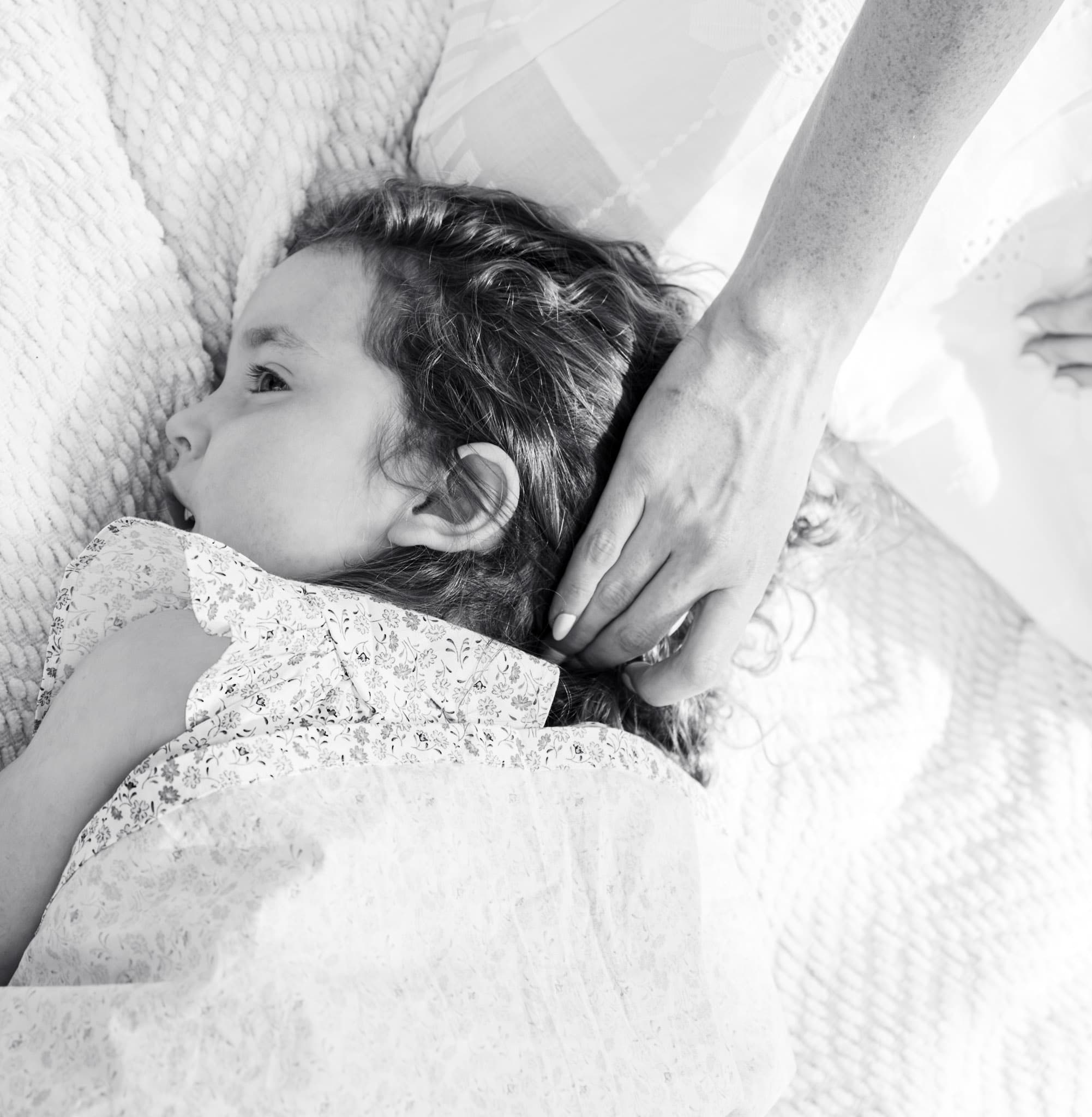 Black and white detail of young girl resting on a quilted blanket with mom's hand stroking her hair