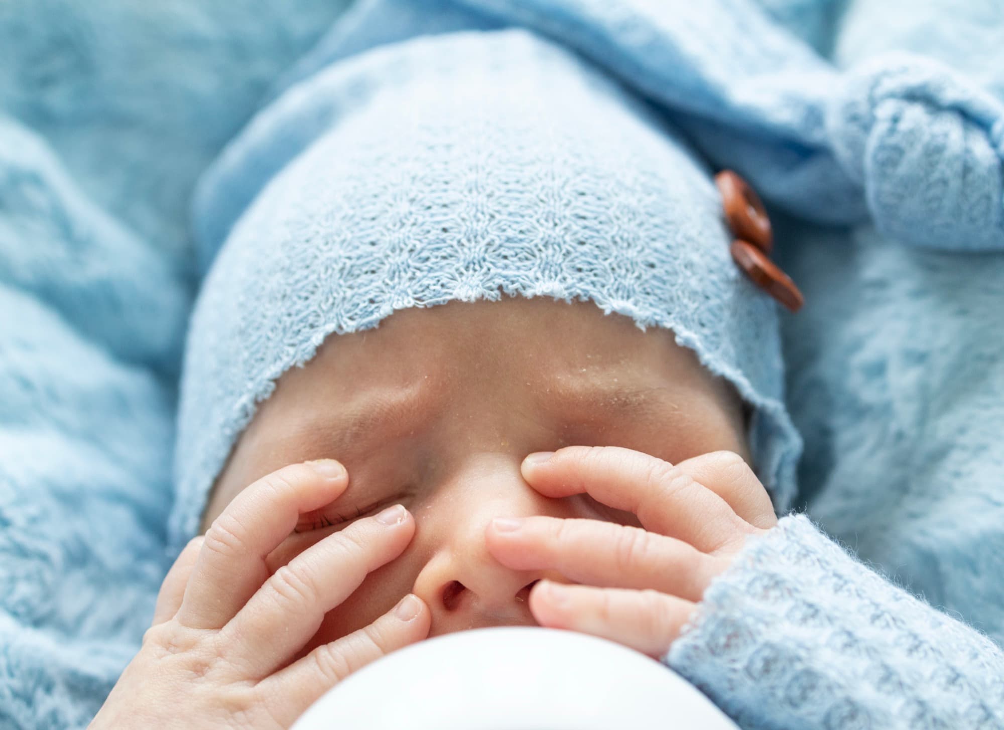 Baby covering face with tiny hands — adorable newborn detail