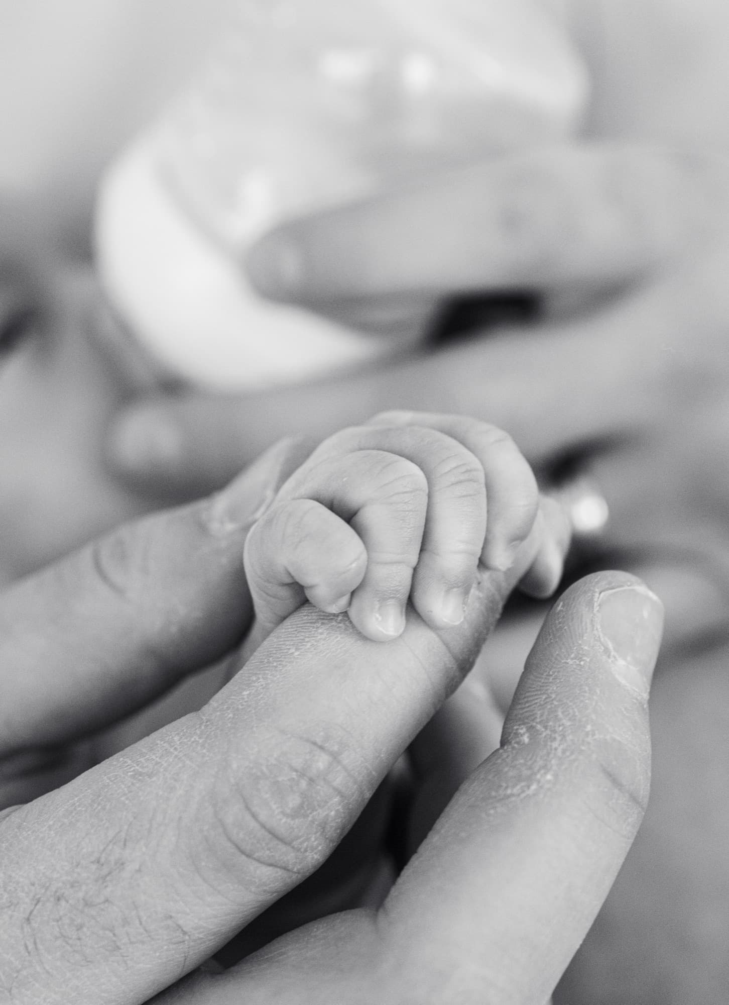 Baby hand gripping parent's finger — black and white newborn detail