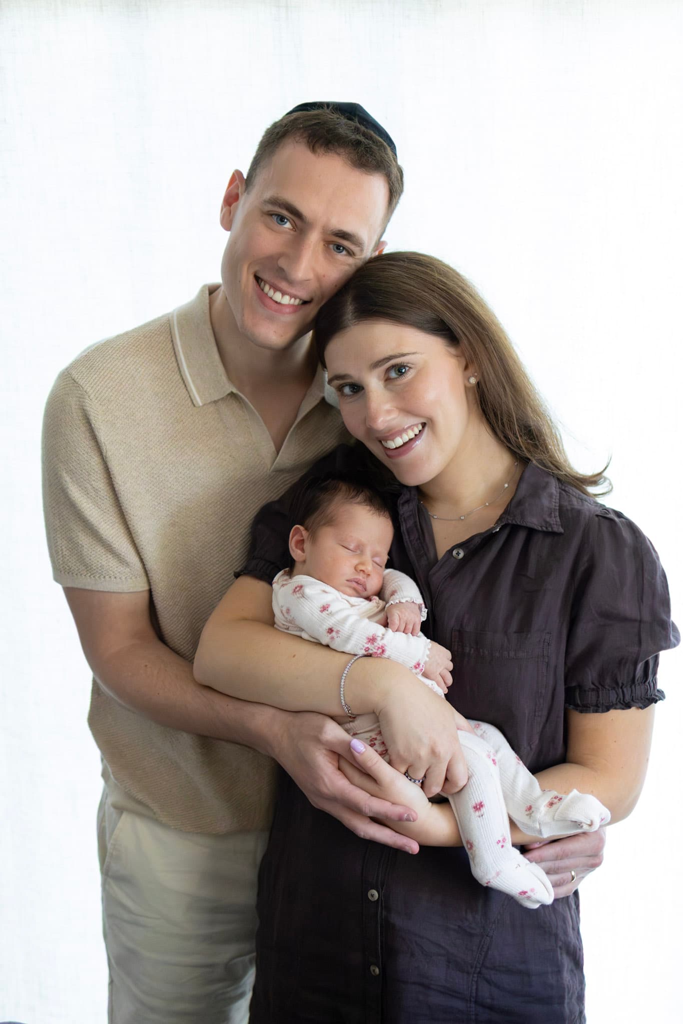 Studio newborn family portrait in Skokie — smiling mom and dad with sleeping baby girl in floral romper