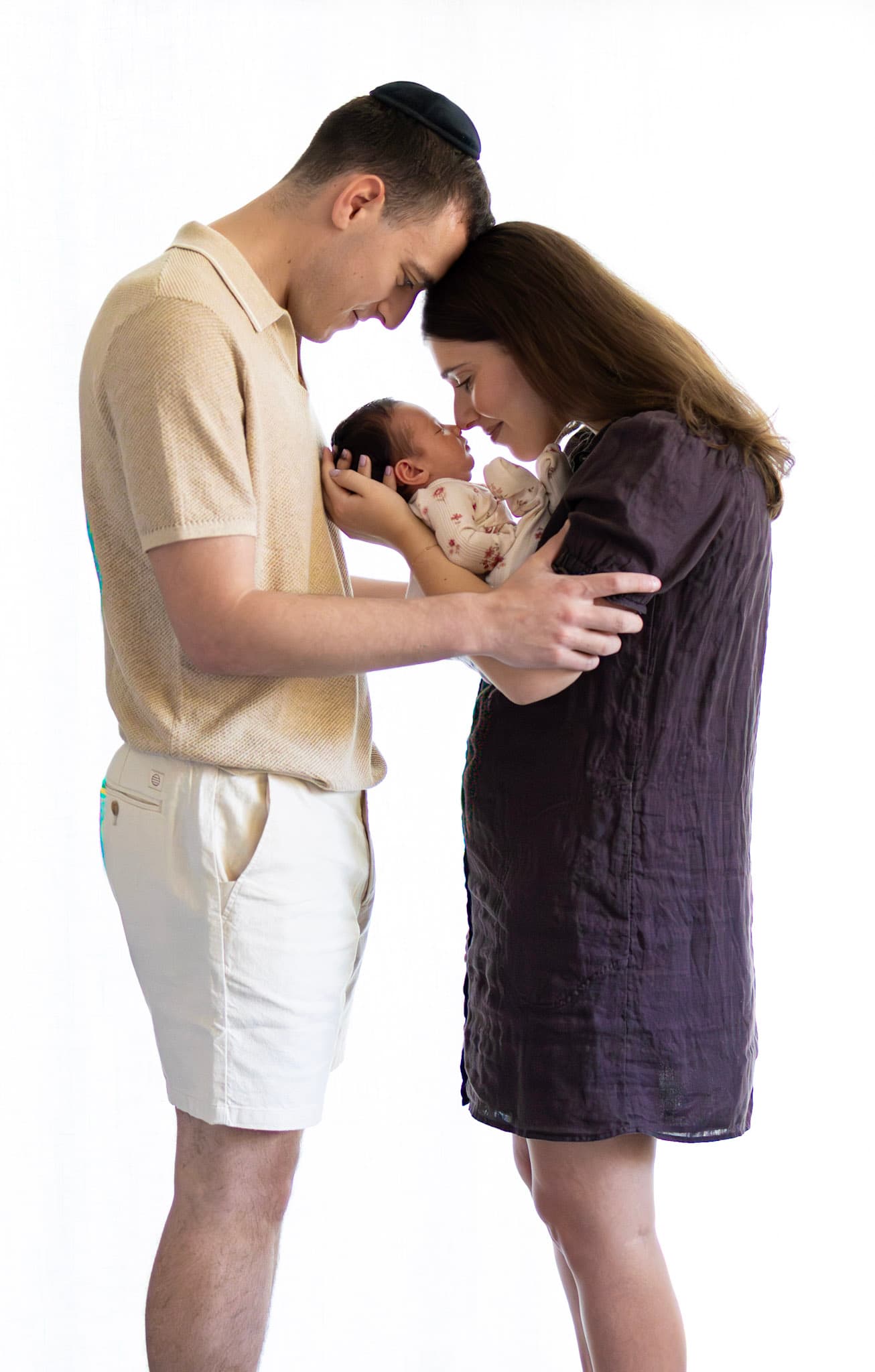 Skokie newborn photography — parents forehead to forehead holding baby girl between them in soft natural light