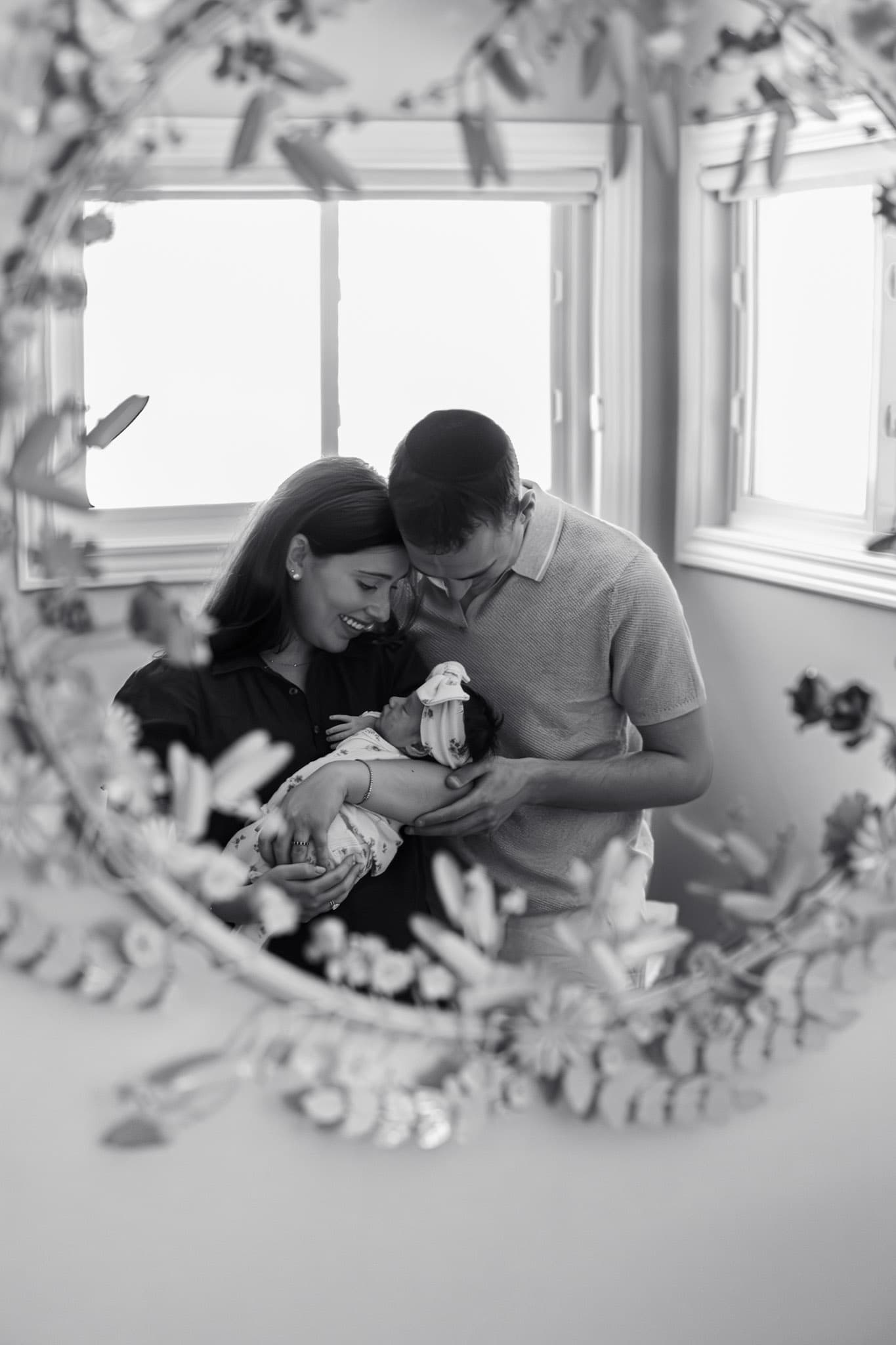 Black and white newborn family photo framed through floral mirror — Skokie in-home newborn photography