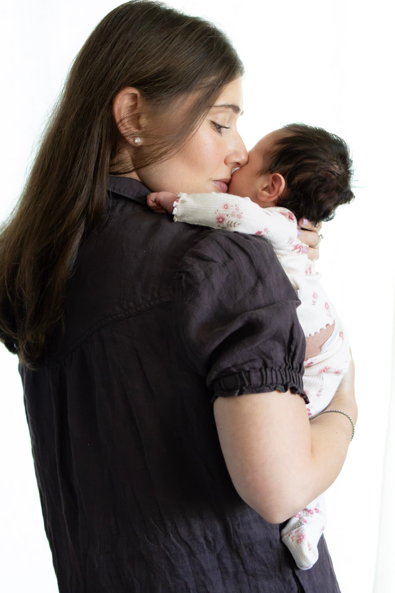 Tender newborn family portrait — parents resting cheeks together holding baby girl in studio light
