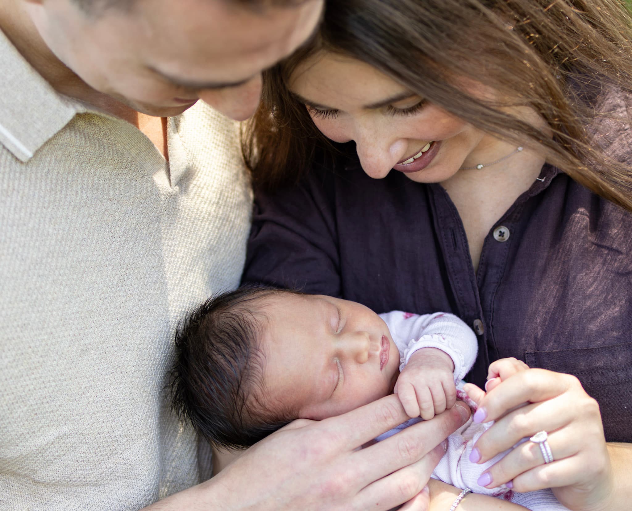 Outdoor newborn portrait — parents looking down at baby girl together during a summer session in Skokie