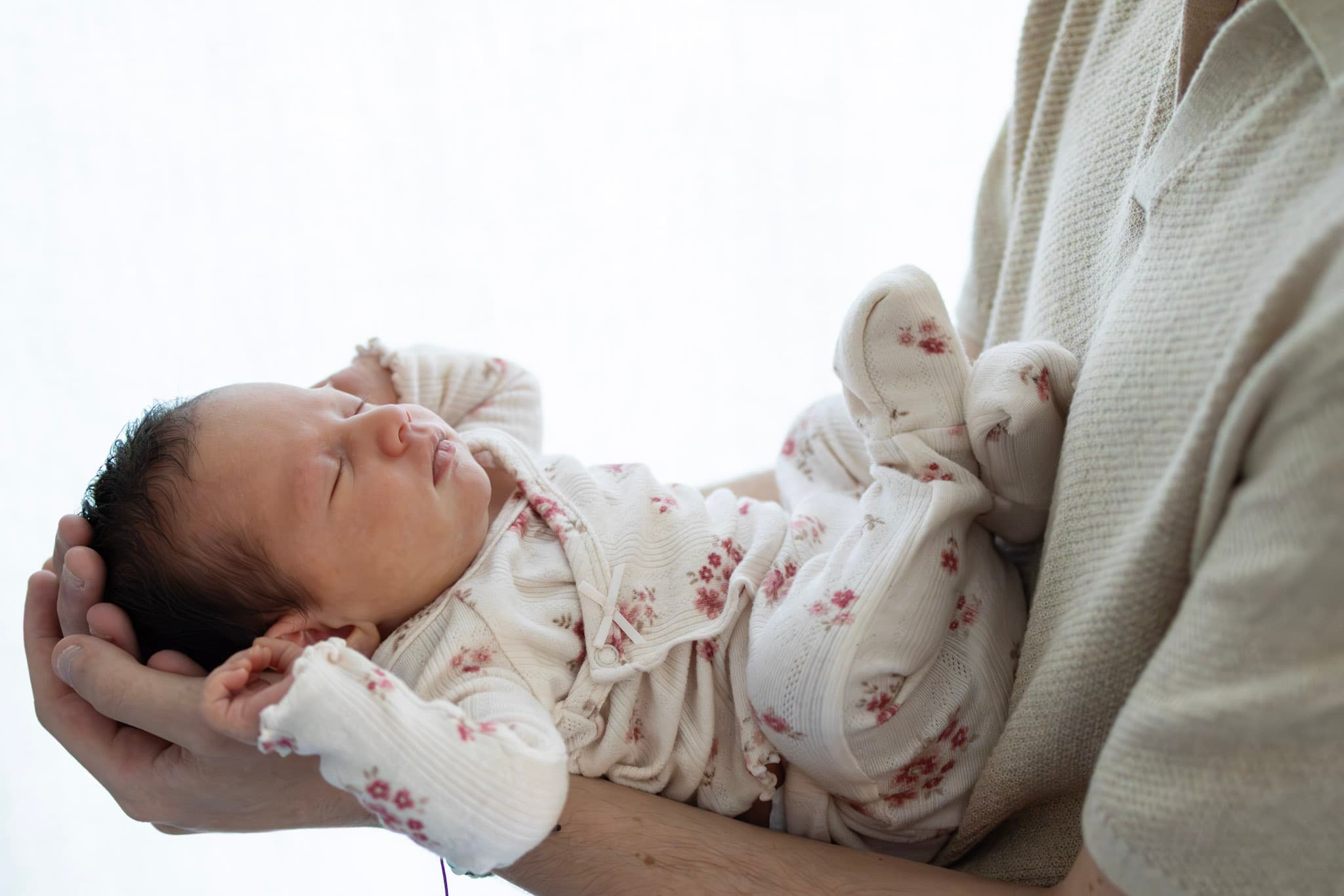 Newborn baby girl resting on parent's forearm in floral outfit — soft natural light detail photo