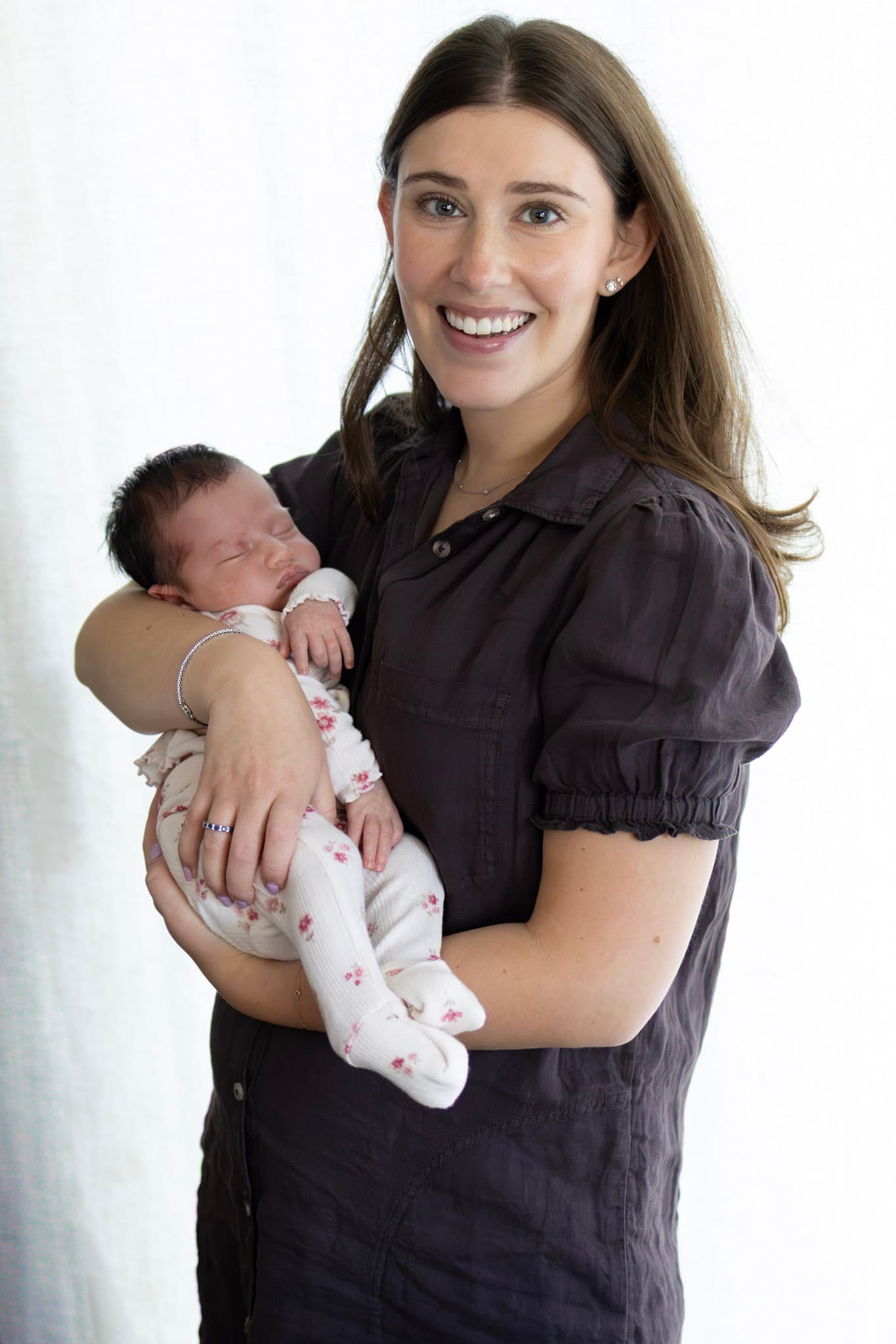 Skokie newborn photography — smiling new mom holding baby girl in front of soft white backdrop