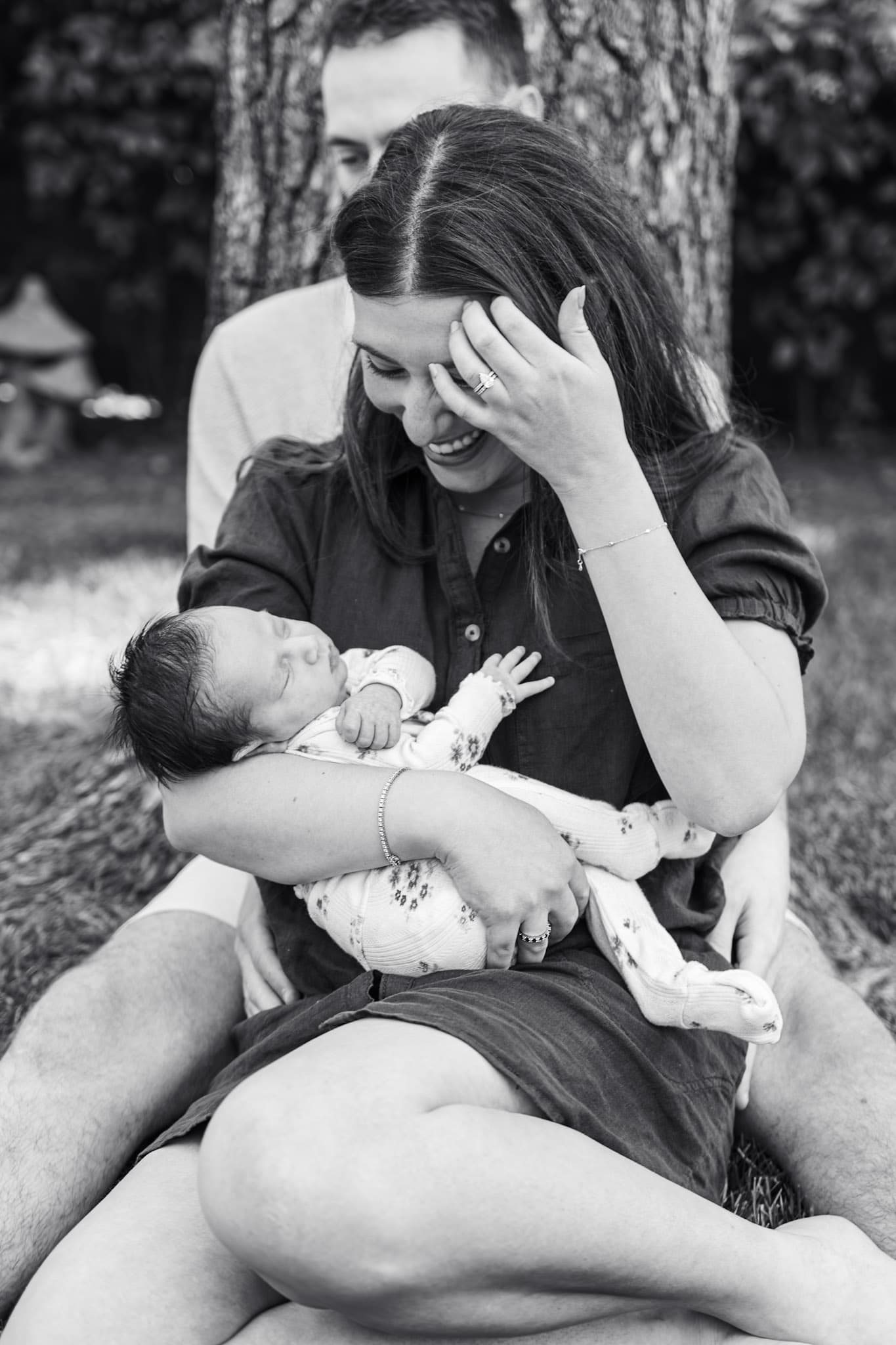 Black and white outdoor newborn portrait — mom laughing while holding baby girl under a tree in Skokie