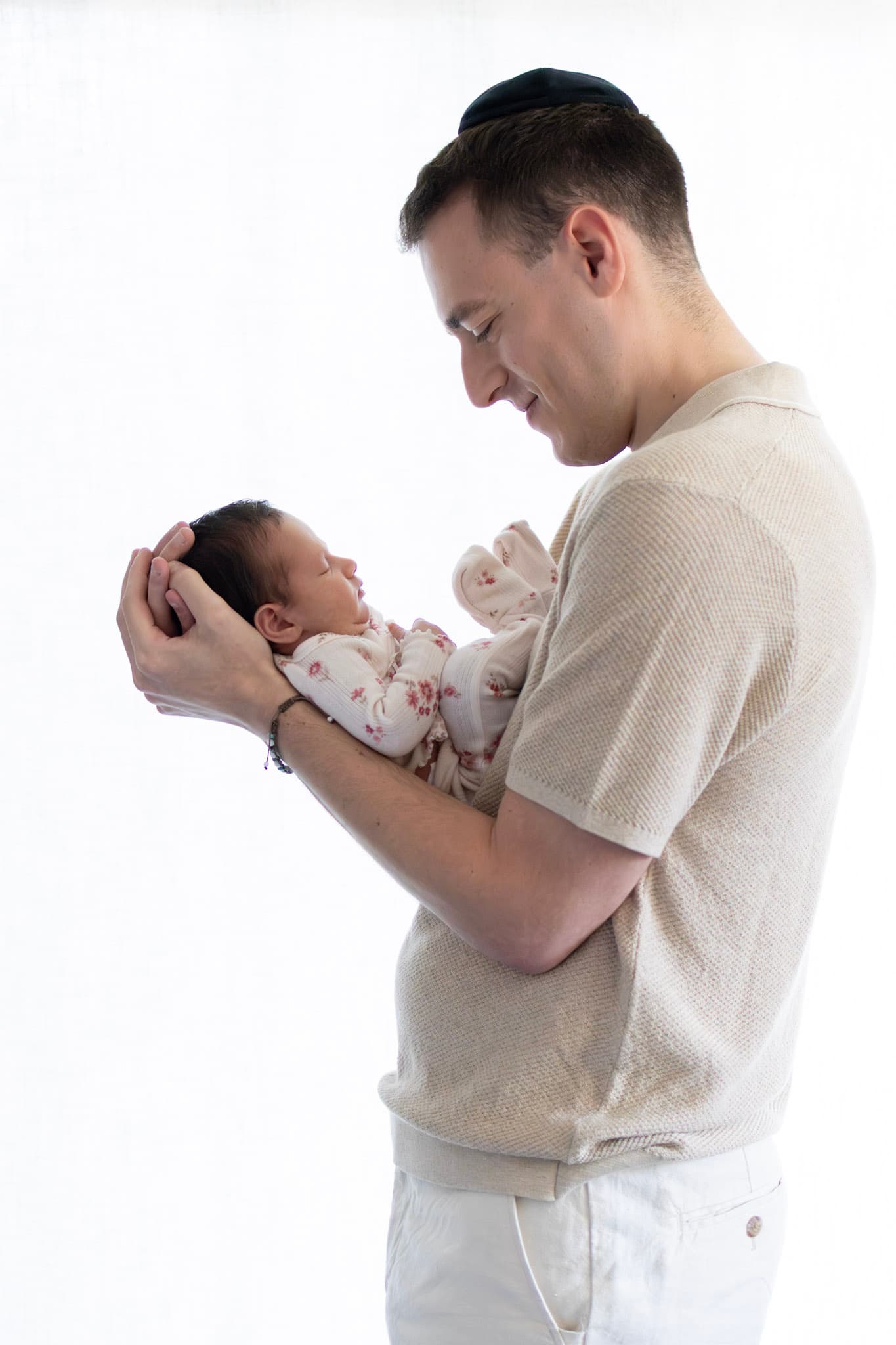 Dad in side profile kissing newborn baby girl's forehead during a soft window-light studio session in Skokie