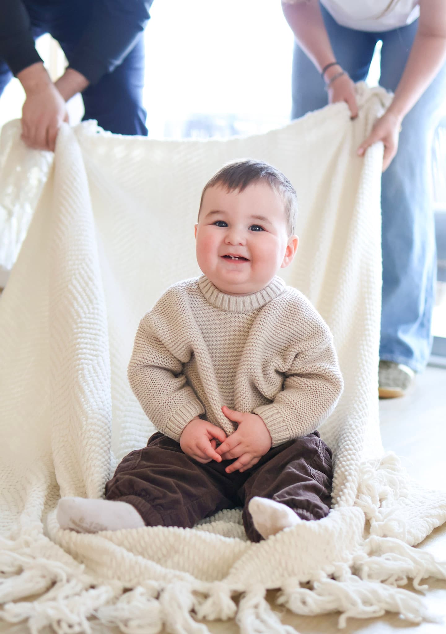 Smiling 9 month old baby sitting on a knit blanket during an in-home family session in West Rogers Park