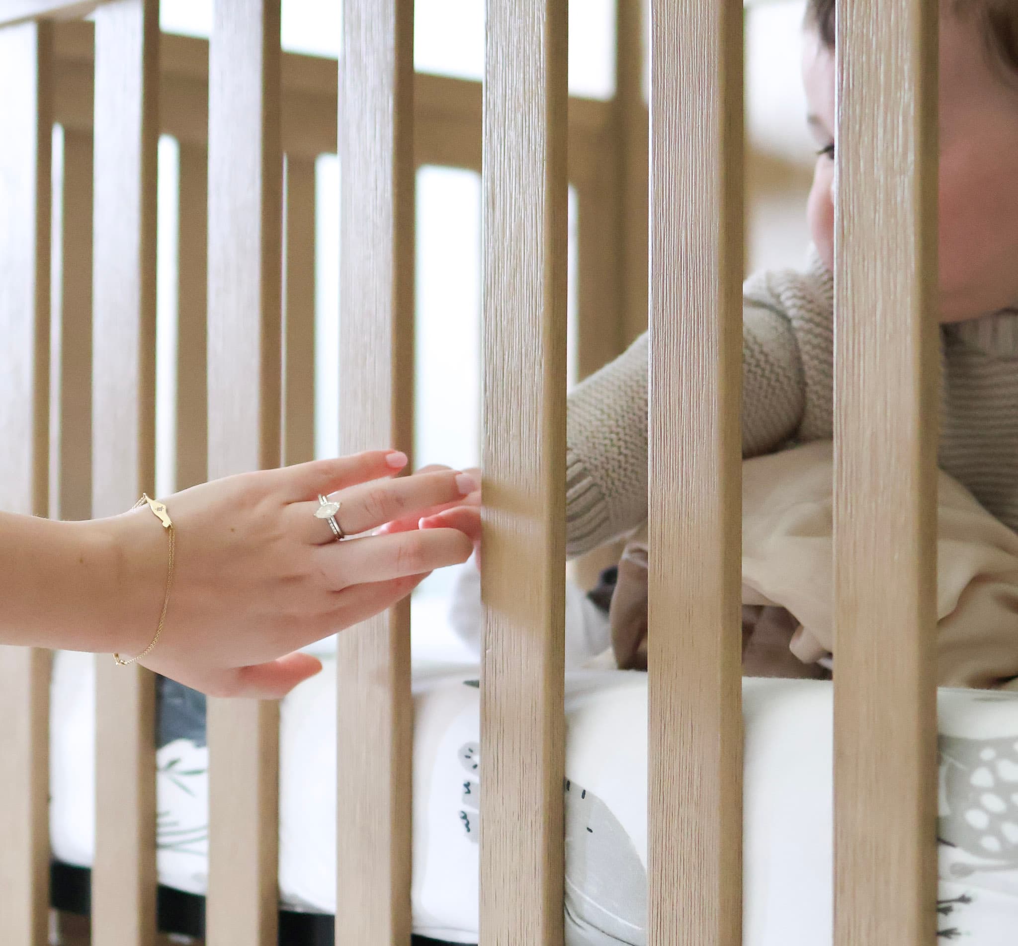Parent reaching for baby through crib slats during a tender at-home family photography moment