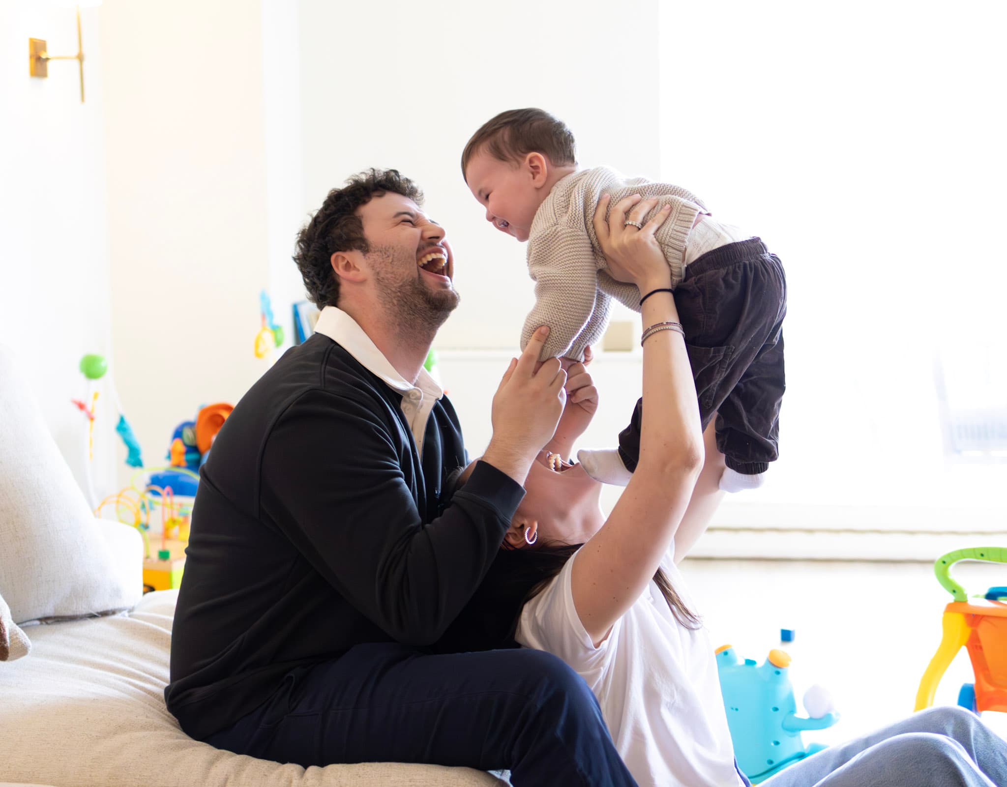 Parents lifting their baby above the couch during a playful in-home family session in West Rogers Park